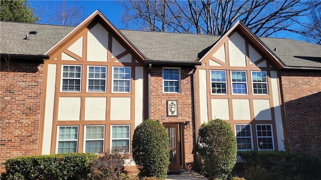 view of front facade with brick siding, roof with shingles, and stucco siding