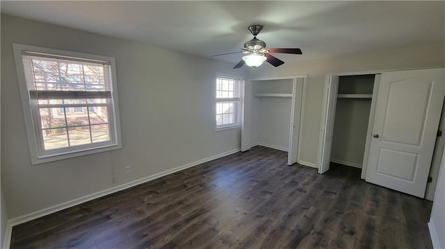 unfurnished bedroom with dark wood-style flooring, two closets, a ceiling fan, and baseboards