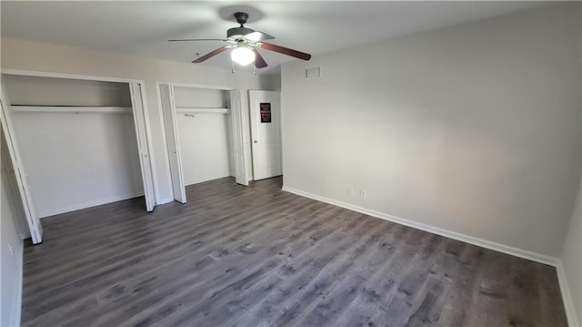 unfurnished bedroom with baseboards, visible vents, a ceiling fan, dark wood-style flooring, and two closets