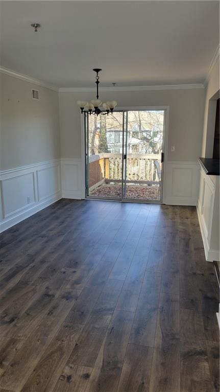 unfurnished dining area with ornamental molding, a chandelier, dark wood-style flooring, and wainscoting