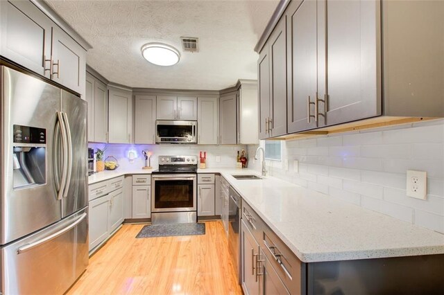 kitchen with gray cabinetry, stainless steel appliances, light wood-type flooring, light stone countertops, and sink