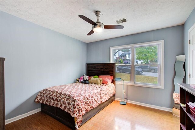 bedroom with hardwood / wood-style flooring, ceiling fan, and a textured ceiling