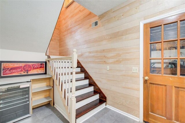 stairs featuring wood walls, beverage cooler, and vaulted ceiling