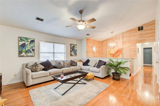 living room with wood walls, vaulted ceiling, hardwood / wood-style flooring, and ceiling fan with notable chandelier