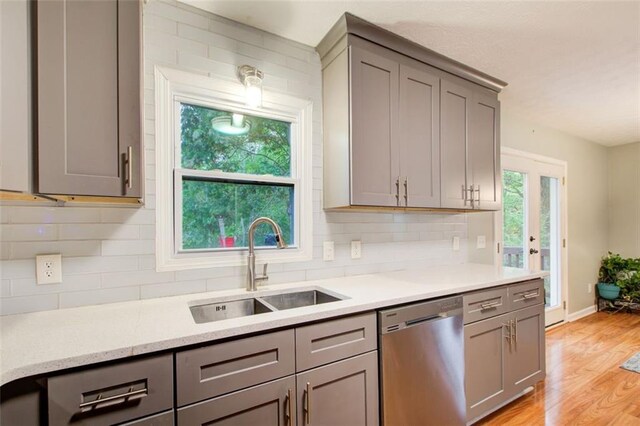 kitchen with tasteful backsplash, stainless steel dishwasher, a wealth of natural light, and light hardwood / wood-style floors