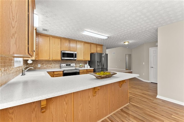 kitchen with sink, stainless steel appliances, a kitchen bar, kitchen peninsula, and light wood-type flooring