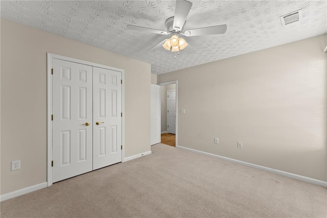 unfurnished bedroom with ceiling fan, light colored carpet, a textured ceiling, and a closet