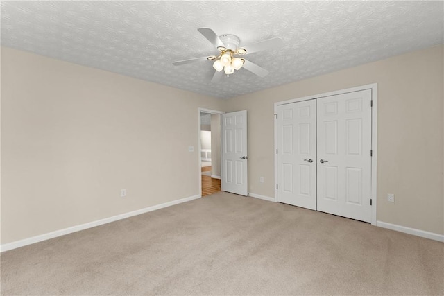 unfurnished bedroom featuring ceiling fan, a closet, light carpet, and a textured ceiling