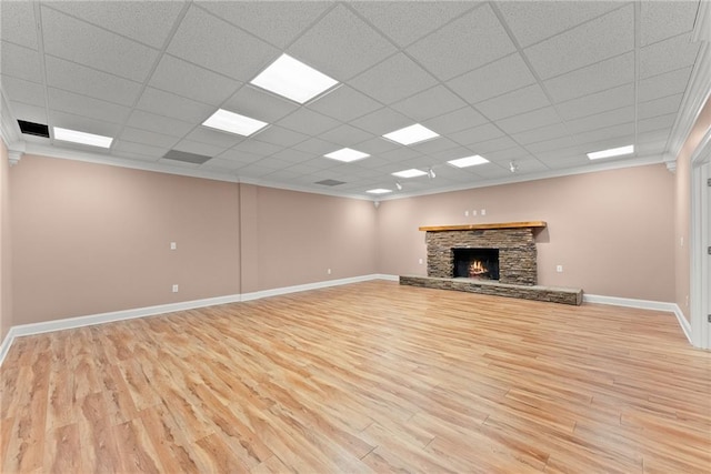 unfurnished living room with crown molding, a stone fireplace, a drop ceiling, and light wood-type flooring