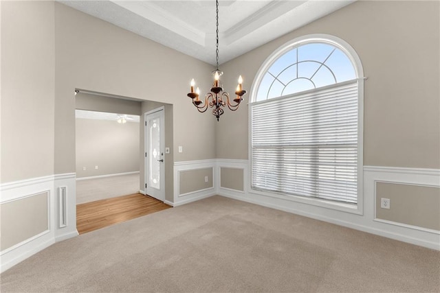 carpeted empty room featuring a raised ceiling and a chandelier