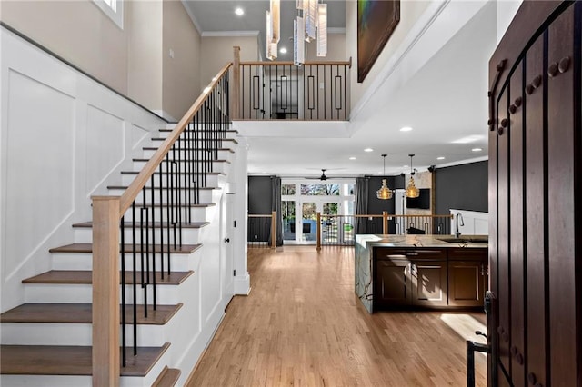 staircase with recessed lighting, ceiling fan with notable chandelier, wood finished floors, a towering ceiling, and crown molding