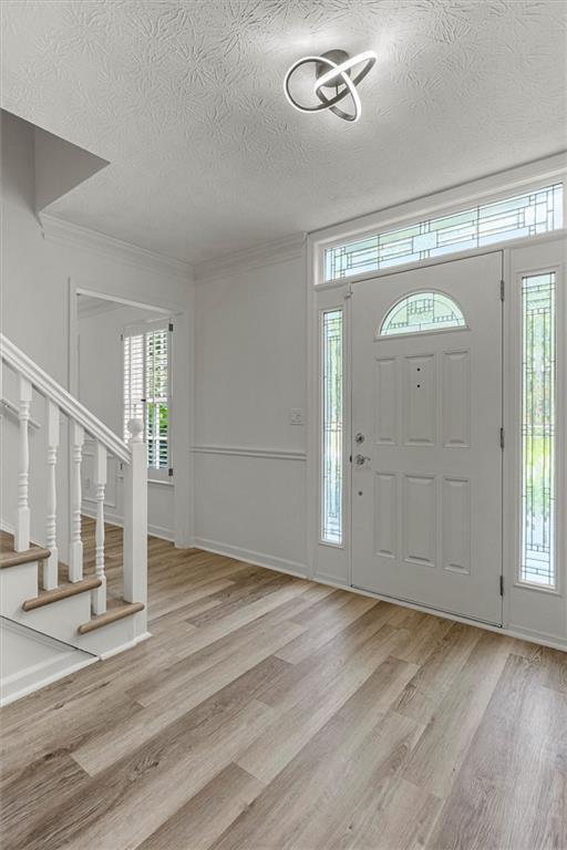 4220 Singing Post Ln NE, Roswell, GA 30075 - foyer entrance featuring light wood finished floors, a textured ceiling, stairway, and crown molding