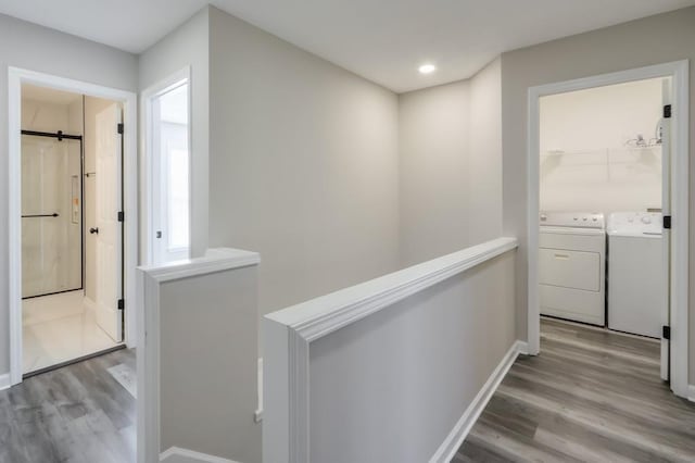 hall featuring light wood-type flooring, washing machine and clothes dryer, an upstairs landing, and baseboards