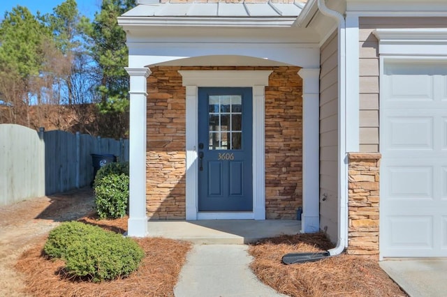 entrance to property featuring a garage, stone siding, and fence