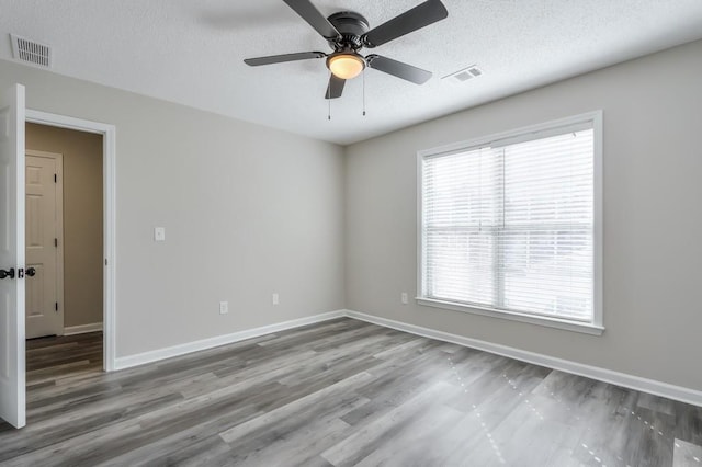 spare room with baseboards, a textured ceiling, visible vents, and wood finished floors