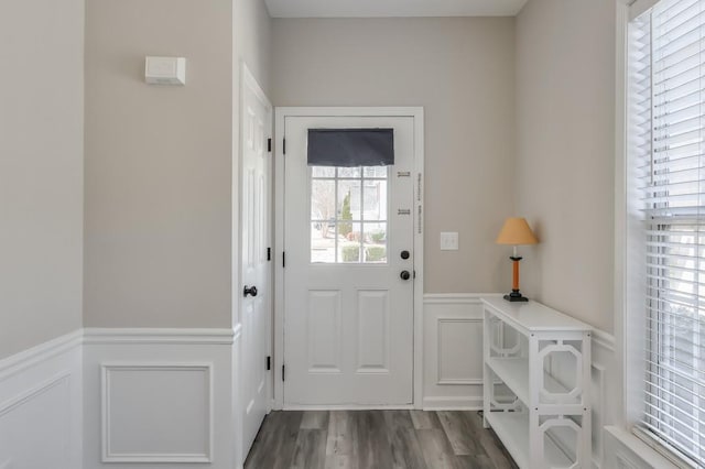 doorway featuring dark wood-style floors, wainscoting, and a decorative wall