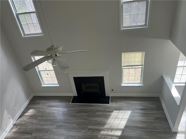 unfurnished living room with a healthy amount of sunlight, dark wood-type flooring, ceiling fan, and a towering ceiling