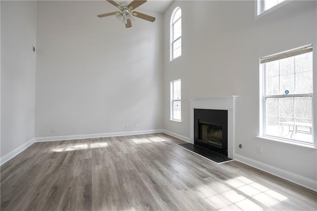 unfurnished living room with a fireplace with raised hearth, a high ceiling, wood finished floors, and baseboards