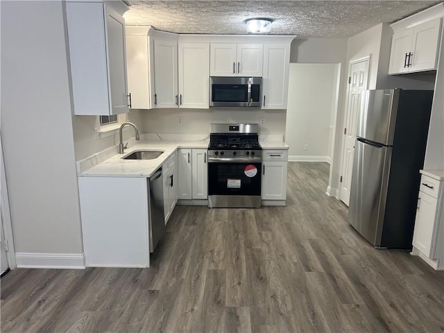 kitchen with appliances with stainless steel finishes, white cabinetry, sink, dark wood-type flooring, and a textured ceiling