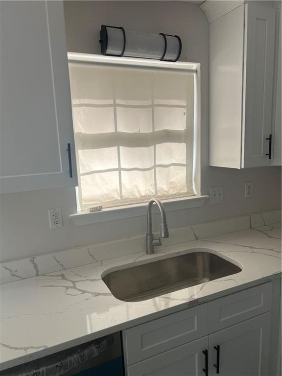 kitchen with white cabinetry, black dishwasher, sink, and light stone counters