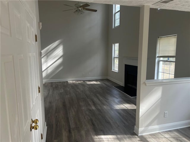 unfurnished living room with dark wood-type flooring, plenty of natural light, ceiling fan, and a high ceiling