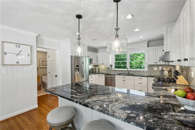 kitchen with stainless steel appliances, a sink, a peninsula, crown molding, and wood finished floors