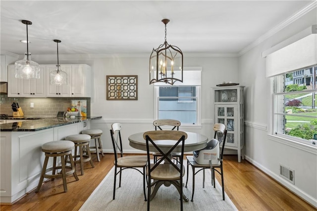 dining space with light wood finished floors, a chandelier, crown molding, and baseboards
