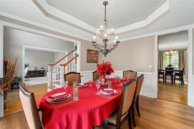 dining area featuring a chandelier, crown molding, wood finished floors, a raised ceiling, and stairs
