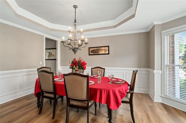 dining room featuring a chandelier, wood finished floors, a tray ceiling, ornamental molding, and a wainscoted wall