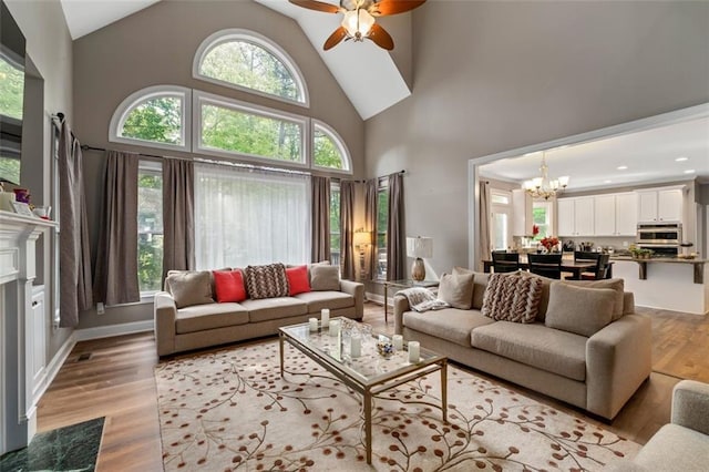 living room featuring a chandelier, high vaulted ceiling, ceiling fan, and light wood-style flooring