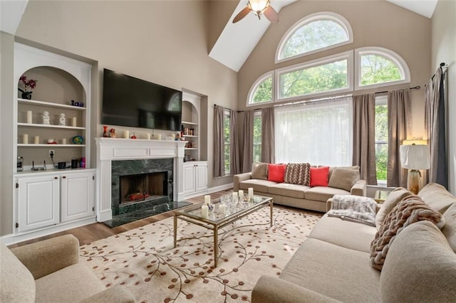 living area with wood finished floors, a ceiling fan, a fireplace, high vaulted ceiling, and built in shelves