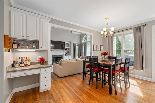 dining area with ornamental molding, a chandelier, light wood finished floors, a high end fireplace, and baseboards