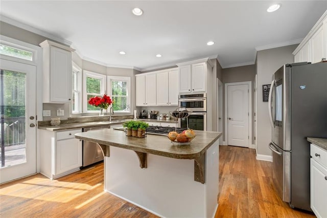 kitchen featuring appliances with stainless steel finishes, ornamental molding, white cabinetry, a kitchen island, and light wood-style flooring
