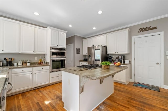 kitchen with stainless steel appliances, crown molding, a center island, white cabinets, and light wood-style flooring