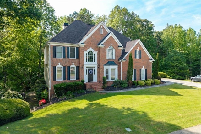 colonial inspired home with brick siding, a chimney, and a front lawn