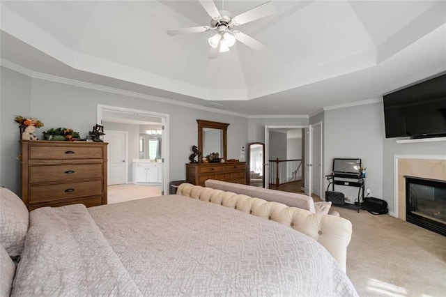 bedroom featuring carpet floors, a raised ceiling, a glass covered fireplace, ornamental molding, and ensuite bath