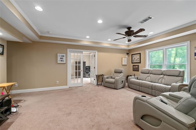 living room with ornamental molding, a raised ceiling, light colored carpet, baseboards, and a ceiling fan