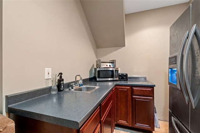 kitchen featuring appliances with stainless steel finishes, a sink, dark countertops, and reddish brown cabinets