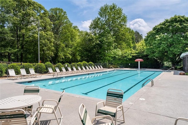 community pool featuring fence, a patio area, and view of wooded area