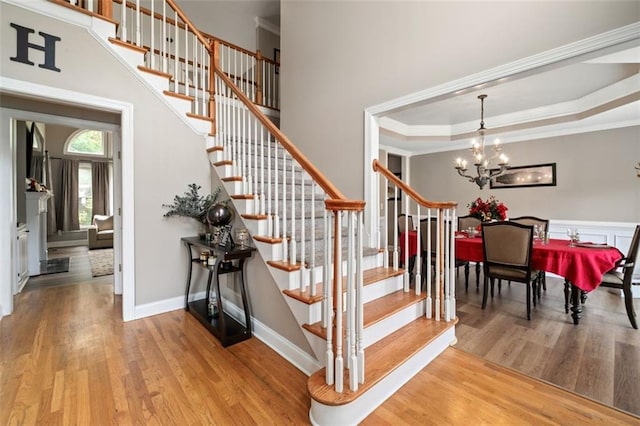 stairway featuring wood finished floors, a chandelier, ornamental molding, and baseboards