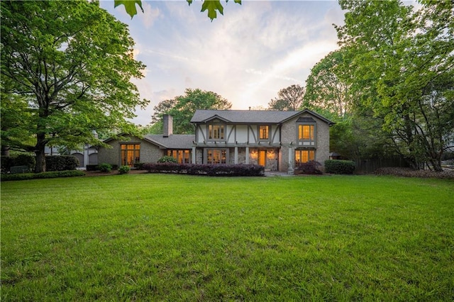 back of property at dusk featuring a lawn and a chimney