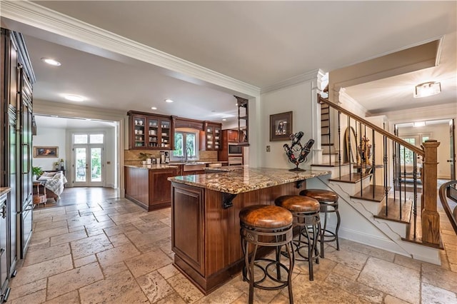 kitchen featuring glass insert cabinets, ornamental molding, a breakfast bar, and stone tile floors
