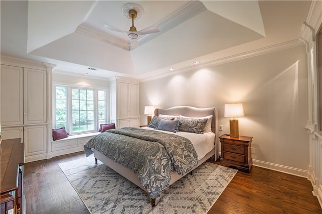 bedroom with crown molding, baseboards, dark wood-type flooring, a tray ceiling, and a ceiling fan