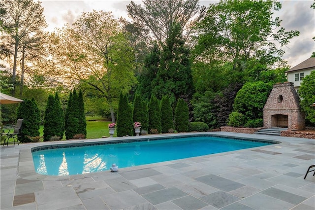 pool with an outdoor fireplace and a patio area