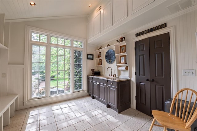 interior space featuring visible vents, lofted ceiling, a decorative wall, a sink, and light tile patterned floors