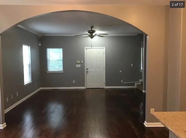 entrance foyer featuring arched walkways, ceiling fan, dark wood-type flooring, baseboards, and ornamental molding