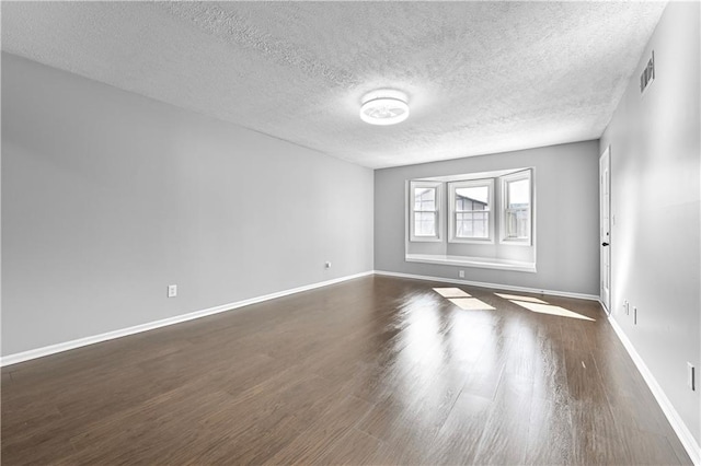 unfurnished room featuring dark wood-style flooring, a textured ceiling, visible vents, and baseboards