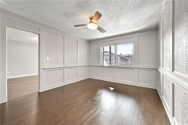spare room featuring ceiling fan, a decorative wall, dark wood-style flooring, and a textured ceiling
