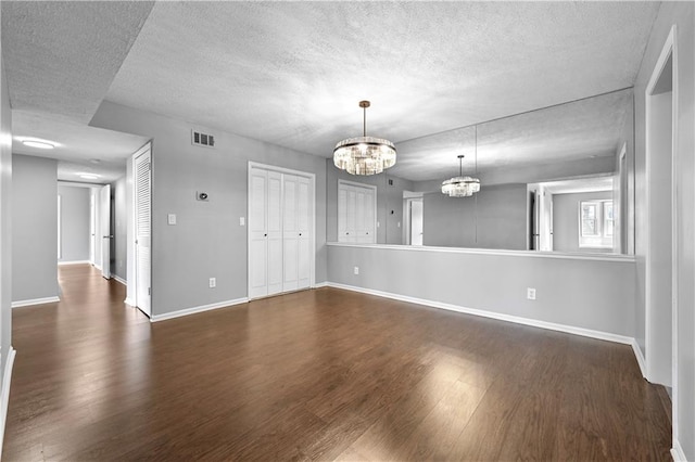interior space featuring a textured ceiling, visible vents, wood finished floors, baseboards, and an inviting chandelier