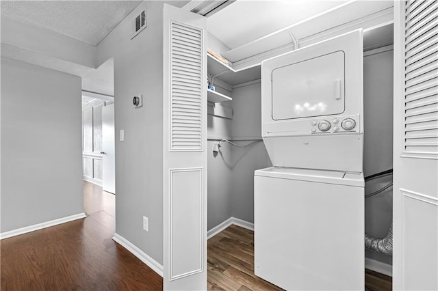 clothes washing area featuring laundry area, stacked washer / dryer, visible vents, wood finished floors, and baseboards